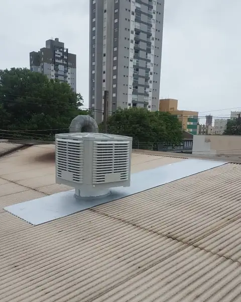 Climatizador com duto de metal no telhado, com prédios ao fundo