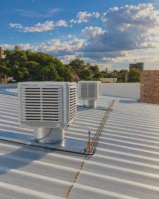 Dois climatizadores no telhado de uma empresa, com céu azul e nuvens